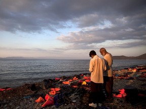 Two Syrian refugees stand on a beach amidst life jackets and deflated dinghies, moments after arriving in a dinghy on the Greek island of Lesbos, on Sept. 13, 2015. (REUTERS/Alkis Konstantinidis)