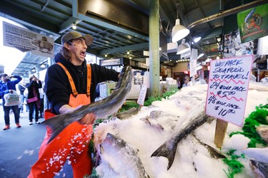 FILE - In this Oct. 3, 2013, file photo, fishmonger Jaison Scott tosses a fresh salmon at the Pike Place Fish Market in Seattle. The market is a classic tourist attraction in Seattle. (AP Photo/Elaine Thompson, File)
