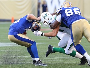 Winnipeg Blue Bombers QB Matt Nichols is brought down by the helmet by Saskatchewan Roughriders DL Alex Hall (not seen) as Bomber OL Stanley Bryant and Rider DL John Chick battle in CFL action during the Banjo Bowl at Investors Group Field in Winnipeg on Sat., Sept. 12, 2015.