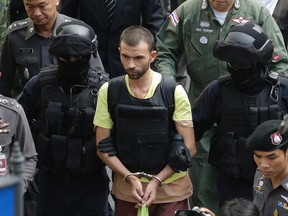 Police officers escort a key suspect in last month's Bangkok bombing, yellow shirt, identified as Adem Karadag, during a re-enactment for the Aug. 17 bombing at Bangkok's popular Erawan Shrine on Sept. 26, 2015. (AP Photo/Sakchai Lalit)