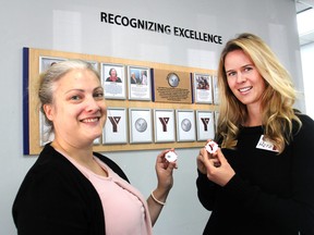Holding Peace it Forward tokens, Nicole Darbey, left, and Kate Lillicrap, from the YMCA of Kingston, stand in front of photos of past winners of the YMCA's annual Peace Medallion award in Kingston Thursday. Nominations for the award are currently open. (Michael Lea/The Whig-Standard)