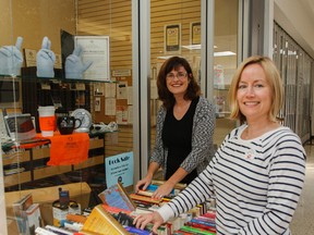Kym Murray, left, and Claire Page, Canadian Hearing Society Kingston’s United Way co-ordinators, organize some books at the sale table outside the hearing society’s office in the Frontenac Mall. The two have organized an ongoing fundraising book sale and one-day garage sale, being held Saturday, to help support local United Way efforts. (Julia McKay/The Whig-Standard)