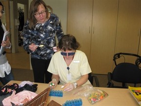 Susan Oster with a participant in the Aging Simulation module of the Alzheimer Information Series. (The participant wears vision inhibiting glasses and gloves with cotton balls in the finger tips and attempts to execute a typical everyday task with simulated physical limitations)