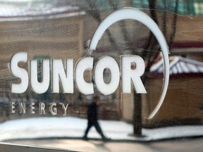 A pedestrian is reflected in a Suncor Energy sign in Calgary, Feb. 1, 2010. Suncor Energy is making a bid to acquire Canadian Oil Sands Ltd., the largest partner in Syncrude. Calgary-based company says it's offering Suncor shares worth about $4.3 billion and would take on about $2.3 billion of debt owed by Canadian Oil Sands, making the total transaction worth $6.6 billion. THE CANADIAN PRESS/Jeff McIntosh