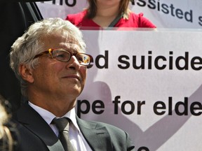 In this file photo, lawyer Joseph Arvay waits to talk to the media as members of the Euthanasia Prevention Coalition protest behind outside the British Columbia Supreme Court in Vancouver. The court in a ruling declared a section of the Criminal Code that prohibits physician-assisted death invalid. Arvay is representing plaintiff Gloria Taylor who suffers from ALS and argued the law infringes on the equality of rights.  
REUTERS