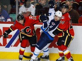 Winnipeg Jets' Alexander Burmistrov, centre, from Russia, gets caught between Calgary Flames Johnny Gaudreau, left, and Jiri Hudler, from the Czech Republic, during NHL pre-season hockey action in Calgary, Saturday, Oct. 3, 2015.THE CANADIAN PRESS/Jeff McIntosh