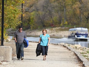 People stroll down the river walk along the Assiniboine River near the Manitoba Legislative Building as a water taxi drives by on an unusually warm Thanksgiving weekend. (Kevin King/Winnipeg Sun/Postmedia Network)