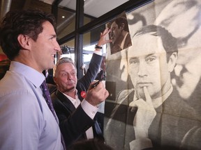 Liberal leader Justin Trudeau looks at a poster of his late father, former Prime Minister Pierre Trudeau, during a campaign stop at a coffee shop in Sainte-Therese, Quebec, October 15, 2015. Canadians will go to the polls in a federal election on October 19. REUTERS/Chris Wattie
