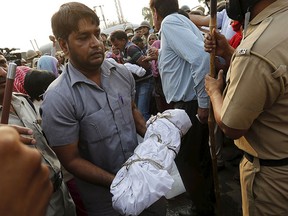 A man carries the body of a child who was burnt alive, wrapped in white shroud, after a protest against the incident at Ballabhgarh, in the northern state of Haryana, India, Oct. 21, 2015. REUTERS/Adnan Abidi