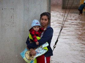 A woman holds her baby in a flooded street as she waits to be taken to a shelter in Zoatlan, Nayarit state, some 150 km northwest of Guadalajara,  Mexico, Saturday, Oct. 24, 2015. Hurricane Patricia made landfall Friday on a sparsely populated stretch of Mexico's Pacific coast as a Category 5 storm, avoiding direct hits on the resort city of Puerto Vallarta and major port city of Manzanillo as it weakened to tropical storm force while dumping torrential rains that authorities warned could cause deadly floods and mudslides. (AP Photo/Eduardo Verdugo)