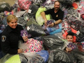 TIM MILLER/THE INTELLIGENCER
Belleville Police Det. Const. Ann Earle-Dempsey. sits in a pile of donated clothes with Stirling-Rawdon Police Const. Scott Burke and Prince Edward OPP Const. Anthony Mann at police headquarters on Thursday in Belleville, Ont. This year's program saw enough to clothe all 1,100 kids in the program.