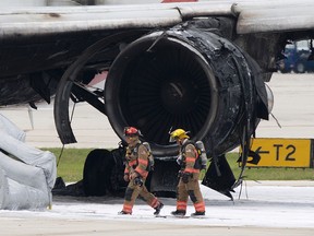 Firefighters walk past a burned engine of an airplane, Thursday, Oct. 29, 2015, at Fort Lauderdale/Hollywood International Airport in Dania Beach, Fla. The passenger plane's engine caught fire Thursday as it prepared for takeoff, and passengers had to quickly evacuate on the runway using emergency slides, officials said. The Dynamic Airways flight was headed to Caracas, Venezuela. (AP/Wilfredo Lee)