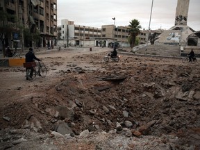 Syrians pass a large hole in the ground reportedly caused by heavy shelling on the rebel-held town of Douma, east of the Syrian capital, on November 4, 2015. The Syrian Observatory for Human Rights said at least 12 people were killed. AFP PHOTO / ABD DOUMANY