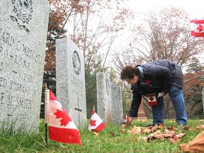 Cathy Semple places a Canadian flag on one of the military graves in  the Cataraqui Cemetery in Kingston on Friday. An unexpectedly large number of volunteers showed up this year to place the flags on the graves. (Michael Lea/The Whig-Standard)