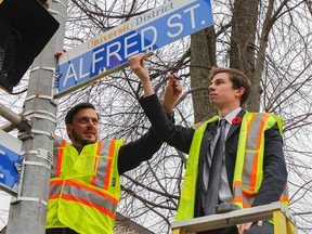 Kingston City Councillor Peter Stroud, left, and Matt Kussin, Queen's Alma Mater Society Municipal Affairs Commissioner, help install a new Alfred Street sign at the intersection of Brock and Alfred streets as part of the University District sign phase two installation in Kingston. (Julia McKay/The Whig-Standard)