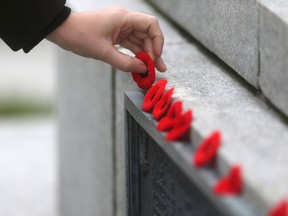 A woman places a poppy on a monument in Winnipeg, following a ceremony at the Legislative Building.  Wednesday, November 11, 2015. (Winnipeg Sun/Postmedia Network)