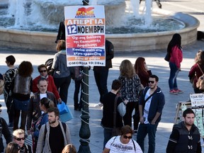 People walk past a placard calling for the November 12th general strike in Athens on November 11, 2015. Greek unions have called a 24-hour general strike -- the first under the leftist government of Alexis Tsipras -- against austerity and further cuts planned under the country's third EU bailout. AFP PHOTO / LOUISA GOULIAMAKI