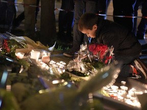 A child puts flowers at a makeshift memorial as people pay homage to attacks' victims near the crime scene of the Bataclan concert hall on November 14, 2015 in Paris, a day after a series of coordinated attacks in and around Paris. Islamic State jihadists claimed a series of coordinated attacks by gunmen and suicide bombers in Paris that killed at least 129 people in scenes of carnage at a concert hall, restaurants and the national stadium. AFP PHOTO / FRANCK FIFE