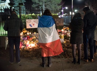 A person wears a French flag at a memorial outside the French Embassy, Saturday, Nov. 14, 2015, in Ottawa, Ontario, following deadly attacks in Paris on Friday. (Justin Tang/The Canadian Press via AP) MANDATORY CREDIT