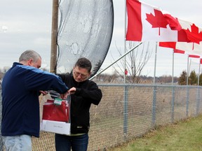 Dianna Cameron and her son James Cameron take down their flag of remembrance in Kingston, Ont. on Saturday November 14, 2015. The Camerons' flag was in honour of Dianna's late husband Sgt. Michael Cameron, an Air Force RADtech 28 years.  Steph Crosier/Kingston Whig-Standard