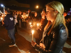 Taylor McMullan, foreground, stands with Molly Gastle, second from right, and Jessica Seemungal at a candlelight vigil behind city hall in Belleville, Ont. Sunday, Nov. 15, 2015. Police estimated close to 200 people attended the vigil for the victims of the Nov. 13 terror attacks in Paris, France.