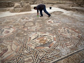 A worker of the Israel Antiquities Authority cleans a 1,700-year-old mosaic, which served as pavement for the courtyard in a villa during the Roman and Byzantine periods, as it is presented to the public and the press for the first time on November 16, 2015, in the Israeli central city of Lod. The scenes in the impressive mosaic depict hunting and hunted animals, fish, flowers in baskets, vases and birds. Another mosaic, which was discovered and excavated in the northern part of the complex in the early 1990s by the late Miriam Avissar, has been exhibited in recent years in some of the world's leading museums, including the Metropolitan, the Louvre and the State Hermitage. AFP PHOTO / MENAHEM KAHANA