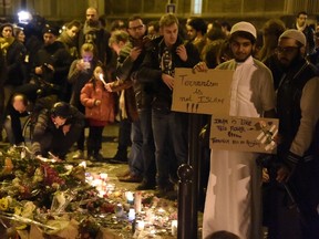 A muslim holds placard reading "Terrorism is not Islam. Islam is like this flower. Terrorism has no religion" during a gathering at "Le Carillon" restaurant one of the site of the attacks in Paris, on November 15, 2015, in the 10th district of Paris. Islamic State jihadists claimed a series of coordinated attacks by gunmen and suicide bombers in Paris that killed at least 129 people in scenes of carnage at a concert hall, restaurants and the national stadium. AFP PHOTO / DOMINIQUE FAGET