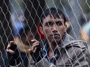 A migrant stands behind a fence, near the northern Greek village of Idomeni, on Wednesday, Nov. 25, 2015. Several European countries, including EU members Slovenia and Croatia and non-members Serbia and Macedonia, have declared they will only allow