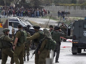 Palestinian youths look from afar as Israeli soldiers gather at the site of a stabbing attack at Al-Fawwar junction near the flashpoint city of Hebron on November 25, 2015. A Palestinian stabbed an Israeli soldier in the southern West Bank and was shot, police and the army said, with medics saying a 20-year-old victim was seriously wounded. AFP PHOTO/HAZEM BADER