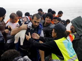 A volunteer (R) asks a Syrian refugee to hand over his child as they arrive aboard a raft at a beach on the Greek island of Lesbos October 23, 2015. Over half a million refugees and migrants have arrived by sea in Greece this year and the rate of arrivals is rising, in a rush to beat the onset of freezing winter, the United Nations said. REUTERS/Yannis Behrakis