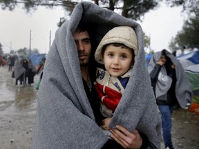 A Syrian refugee carries his son through a rainstorm as he arrives at the Greek-Macedonian border near the Greek village of Idomeni November 27, 2015. Picture taken from the Greek side of the border. REUTERS/Yannis Behrakis