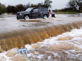 Two people push a vehicle out of high water at Cal Young Park, Sunday, Nov. 29, 2015, in Abilene, Texas. A deadly storm that has caused flooding and coated parts of the southern Plains in ice during the Thanksgiving holiday weekend dumped more rain on already swollen rivers in parts of North Texas and Arkansas on Sunday and made driving dangerous in parts of Oklahoma. (Ronald W. Erdrich/The Abilene Reporter-News via AP)