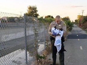 This Friday, Nov. 27, 2015 file photo provided by the Los Angeles County Sheriff's Department shows Deputy Adam Collette holding an infant girl where she was found abandoned under asphalt and rubble, near a bike path in Compton, Calif., as they seek the public's help in identifying her. Collette, who dug the abandoned newborn girl out of a hole, says he believes the infant had “a touch of God that day” to survive. Doctors say the baby might have died within hours, but she's now stable and healthy at a hospital. Officials are asking the unknown mother to come forward. (Los Angeles County Sheriff's Department via AP, File)