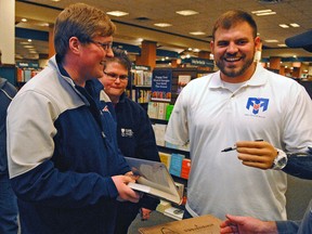 Travis Mills, right, jokes around with customers while autographing a copy of his book "Tough As They Come" on Tuesday, Dec. 1, 2015, at a Barnes and Noble store in Augusta, Maine. Mills, 28, who was an Army staff sergeant when he lost all four limbs during an explosion in Afghanistan, aims to inspire others with his story. (Joe Phelan/The Kennebec Journal via AP)