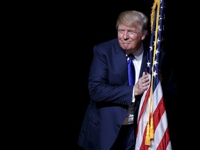 U.S. Republican presidential candidate Donald Trump hugs a U.S. flag as he takes the stage for a campaign town hall meeting in Derry, N.H., in this Aug. 19, 2015 file photo. (REUTERS/Brian Snyder)