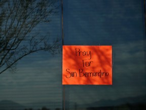 A sign asking for prayers is posted on the window of an office building near a makeshift memorial site honoring the victims of Wednesday's shooting rampage Friday, Dec. 4, 2015, in San Bernardino, Calif. The FBI said Friday it is officially investigating the mass shooting in California as an act of terrorism, while a U.S. law enforcement official said the woman who carried out the attack with her husband had pledged allegiance to the Islamic State group and its leader on Facebook. (AP Photo/Jae C. Hong)