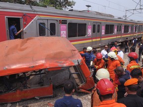 Rescuers remove the wreckage of a passenger minibus after it was hit by a commuter train in Jakarta, Indonesia, Sunday, Dec. 6, 2015. Police say the train slammed into the bus at a railroad crossing killing and injuring number of people. (AP Photo)