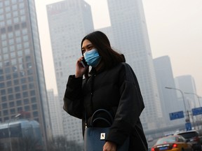 A woman wearing a mask to protect herself from pollutants walks past office buildings shrouded with pollution haze in Beijing, on Dec. 7, 2015. (AP Photo/Andy Wong)