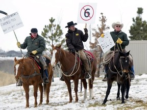 Ranchers on horseback raise signs to protest Bill 6 at a meeting in Okotoks December 2, 2015 with provincial Labour Minister Lori Sigurdson and Agriculture Minister Oneil Carlier. Alberta's government will retool a bill that would overhaul workplace standards on farms in Canada's biggest cattle-producing province, its agriculture minister said, after protests by farmers and ranchers.  REUTERS/Mike Sturk