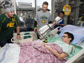 Eskimos quarterback Mike Reilly, right, and kicker Grant Shaw bring the Grey Cup to patient Cody Carson in the Stollery Children's Hospital last Friday. (David Bloom, Edmonton Sun)