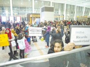 Members of groups sponsoring two Syrian refugee families hold up signs welcoming their charges as they wait for the families to arrive at Toronto?s Pearson Airport, on Wednesday. (Chris Young/The Canadian Press)