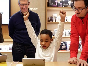 In this Wednesday, Dec. 9, 2015, file photo, third-grader Jaysean Erby raises his hands as he solves a coding problem as Apple CEO Tim Cook watches from behind during a coding workshop at an Apple Store, in New York.  (AP Photo/Mark Lennihan, File)
