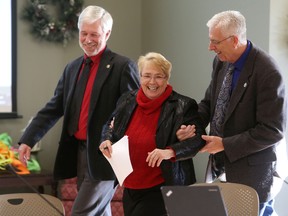North Frontenac Mayor Ron Higgins, left, and South Frontenac Mayor Ron Vandewal escort Central Frontenac Mayor Frances Smith to the head of the Frontenac County council table after she was acclaimed as county warden on Wednesday in Glenburnie. (Elliot Ferguson/The Whig-Standard)