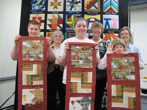 Participants in a learn-to-quilt program that recently took place at the Chatham branch of the public library, included, from left, Ryan Heyboer, 13, of Ridgetown, and his mentor and great-aunt Nancy Kominek; Rebecca Osmon, 16, of Chatham, and her mentor Jayne Park; and Keira Knight, 10, of Chatham and her mentor Ruth Roe. The students pose with wall hangings their mentors helped them create. In the background is the People of the Thames quilt recently created by members of the Chatham-Kent Quilters Guild. The panels from that quilt have now been recreated on barns located on the quilt trail along the Thames River.