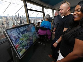 In this Sept. 19, 2014, file photo, Anan Bishara, left, and Denise Burrell, right, both from New York, check out a virtual reality display that lets visitors explore the Pike Place Market and other attractions atop the Space Needle in Seattle. The high-tech attractions are part of an explosion of virtual reality in the travel industry. (AP Photo/Ted S. Warren, File)