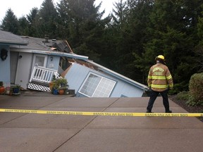 In this Friday, Dec. 18, 2015 photo released by the Newport News-Times, a Newport Firefighter looks at a home that was damaged from storms in Newport, Ore. Fresh storms barreled through the already sodden Pacific Northwest on Friday, triggering a landslide that killed a woman near the Oregon Coast and clogging mountain passes in the Washington Cascades. (Steve Card/Newport News-Times via AP)