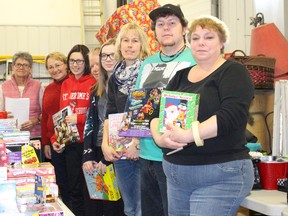 Volunteers for the Santa Anonymous project pose in front of some toys during the last day of collection on Friday, Dec. 18 at the ATCO Gas building.
