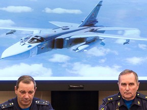 Col. Nikolai Primak, left, head of Russian investigation commission, and Lt-Gen. Sergei Bainetov speak about the Russian Su-24 bomber, seen behind, which was shot down by Turkey at the border with Syria on Nov. 24, saying it violated its airspace for 17 seconds despite repeated warnings, in Moscow on Monday, Dec. 21, 2015.   (AP Photo/Pavel Golovkin)