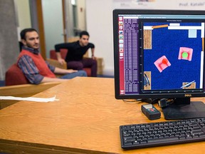 In this Nov. 19, 2015, photo, Massachusetts Institute of Technology researchers Fadel Adib, left, and Emad Farag sit in chairs as a screen displays how RF-Capture is tracking them through the wall behind them on the MIT campus in Cambridge, Mass. RF-Capture is a technology being developed at MIT that uses WiFi signals to see and sense through walls. (AP Photo/Scott Eisen)
