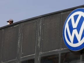 A worker wearing a protective mask stands next to a Volkswagen logo at a dealership in Madrid, Spain, December 16, 2015. (REUTERS/Sergio Perez)